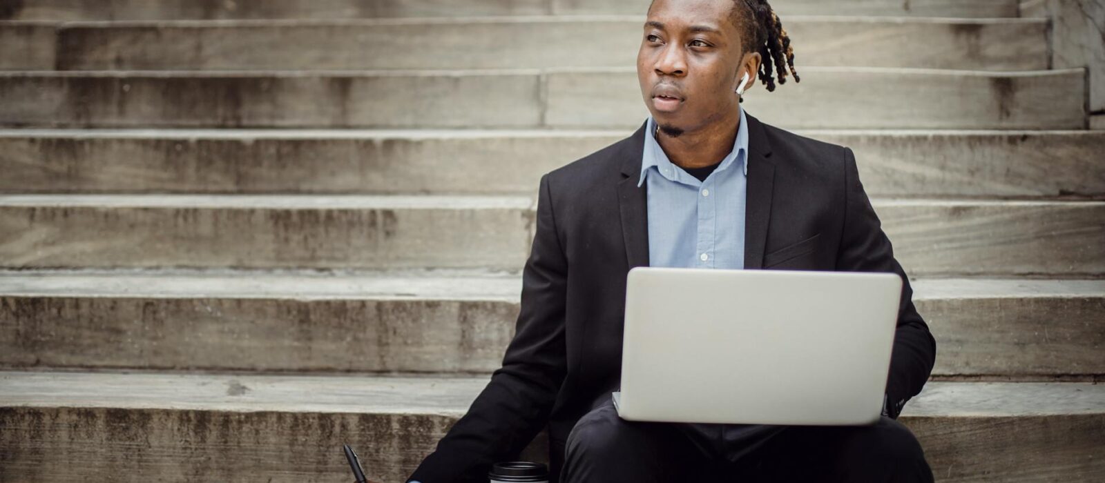 thoughtful black worker using netbook and taking notes sitting on steps